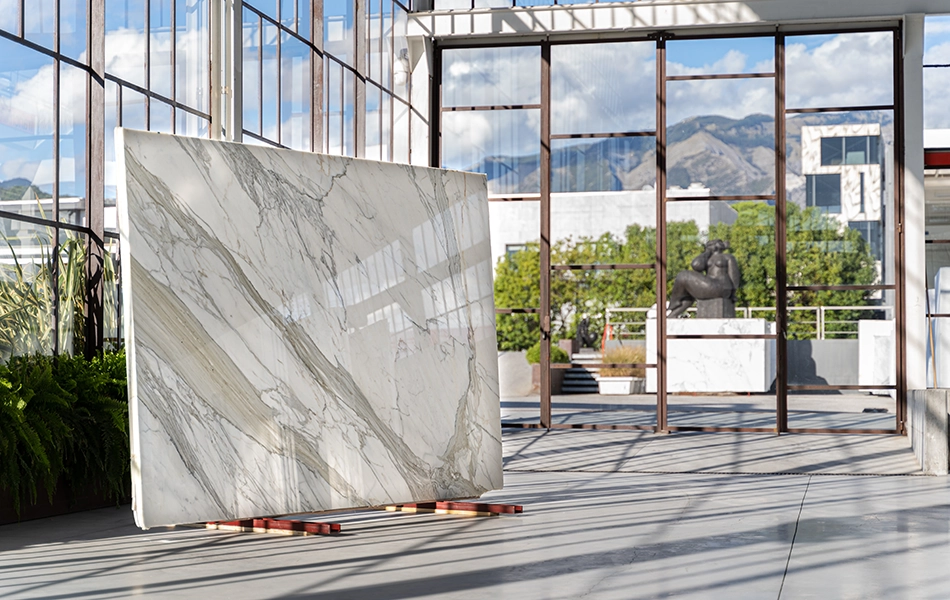 Lastre di marmo bianco con venature grigie e beige esposte in uno showroom moderno, con vetrate e vista sulle montagne.